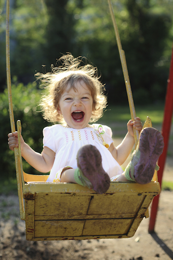 Laughing child on swing in summer park